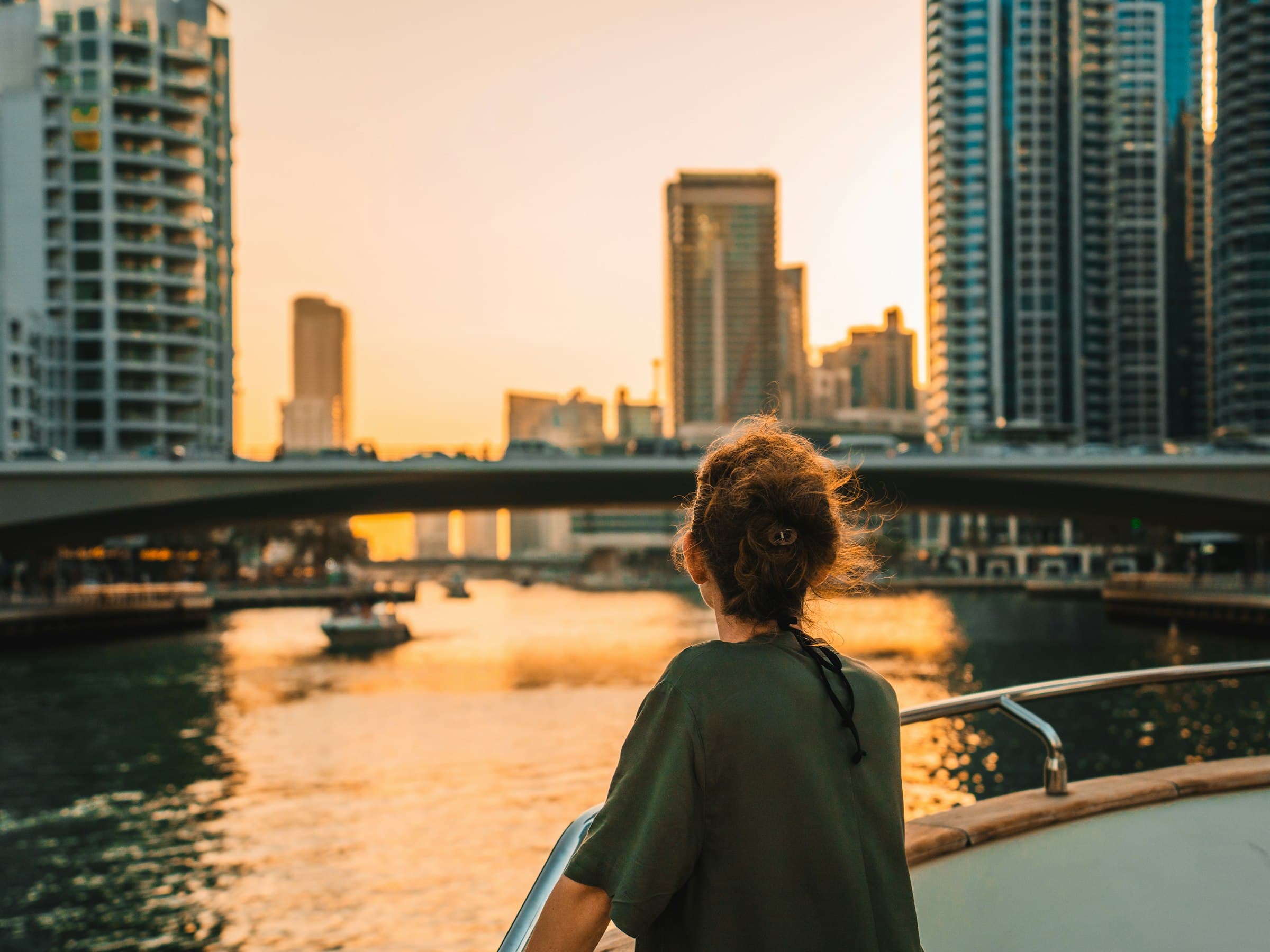 Guest on a boat's bow looking at the Dubai Marina towers and bridge in golden evening light