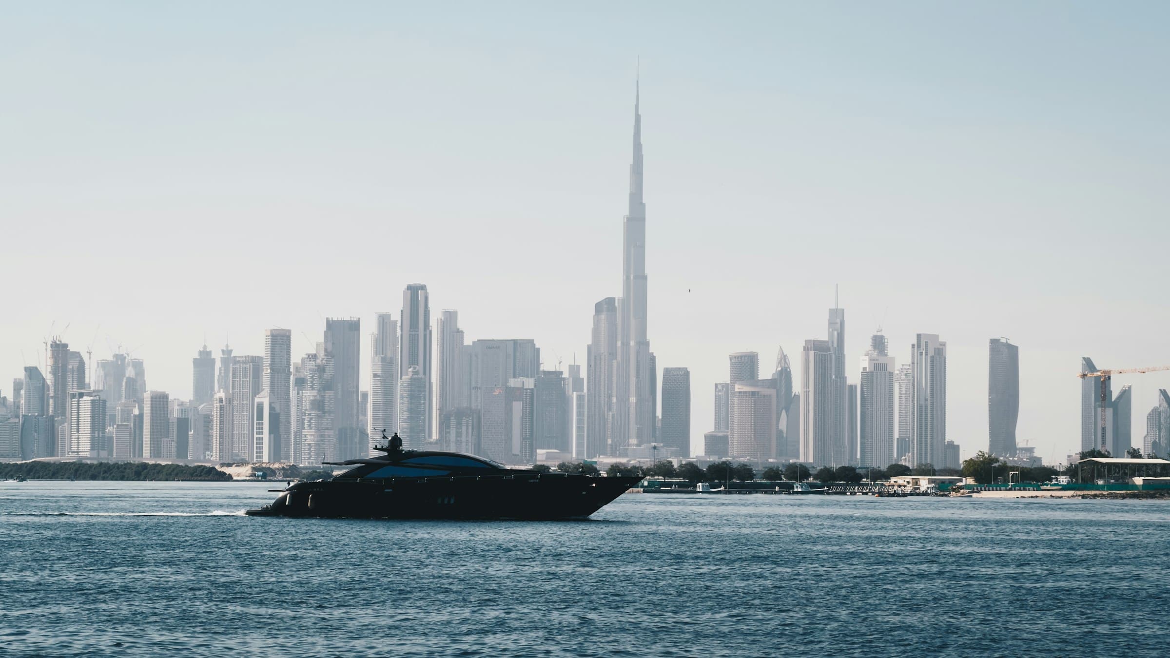 Dark motor yacht underway on open water against the Dubai skyline with Burj Khalifa