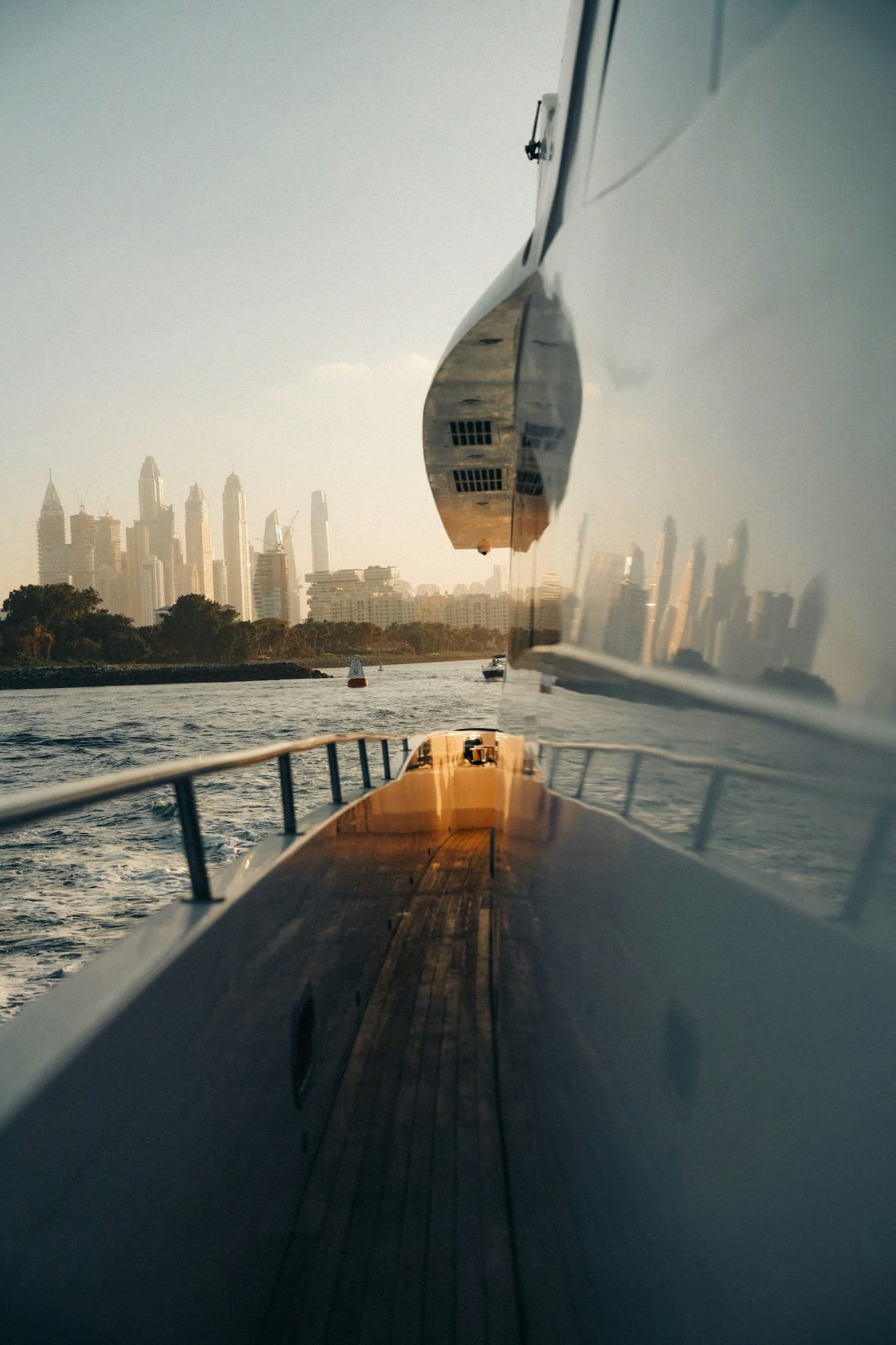 View from a yacht's deck — teak flooring and railing, with the Dubai skyline in golden light